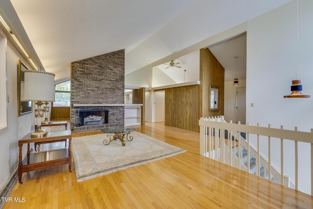 living room with wood-type flooring, high vaulted ceiling, a brick fireplace, and ceiling fan