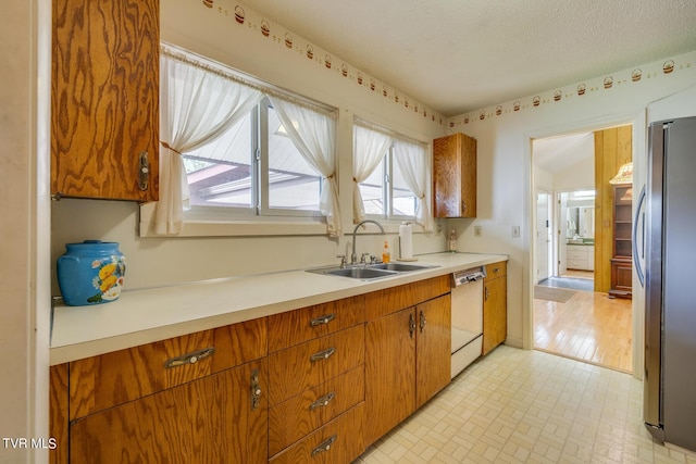 kitchen featuring stainless steel refrigerator, dishwasher, sink, and a textured ceiling