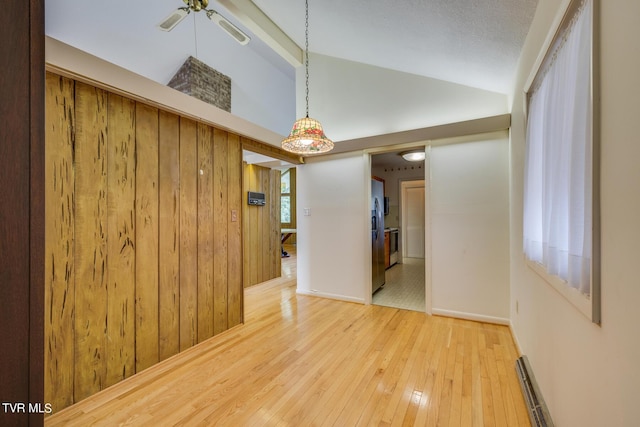 spare room featuring wood walls, a baseboard radiator, wood-type flooring, and vaulted ceiling