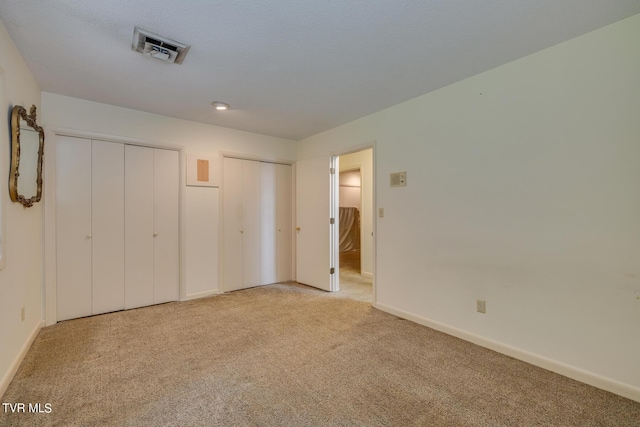 unfurnished bedroom with multiple closets and light colored carpet