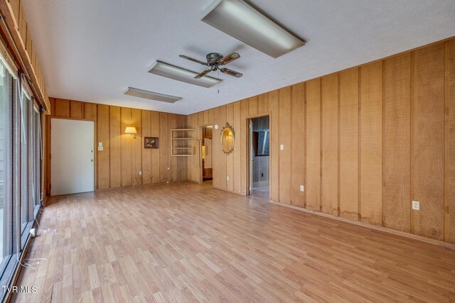 unfurnished living room with ceiling fan, wooden walls, and light hardwood / wood-style flooring