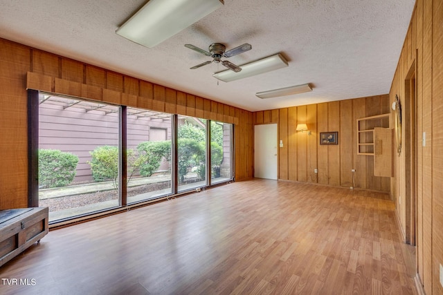 unfurnished living room with ceiling fan, wood walls, light wood-type flooring, and a textured ceiling