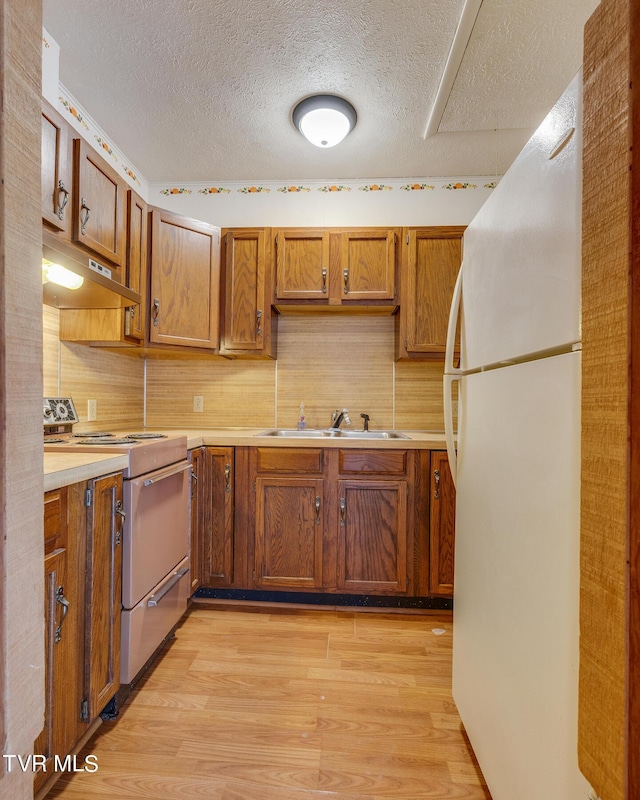 kitchen with a textured ceiling, light hardwood / wood-style flooring, white appliances, and sink