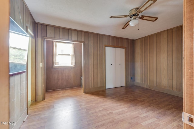 interior space featuring ceiling fan, light wood-type flooring, and wooden walls