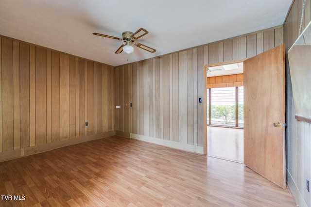 unfurnished room featuring ceiling fan, wooden walls, and light wood-type flooring