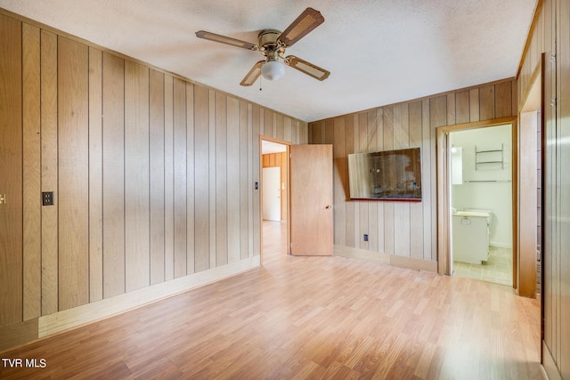 unfurnished room with ceiling fan, wood walls, light hardwood / wood-style floors, and a textured ceiling