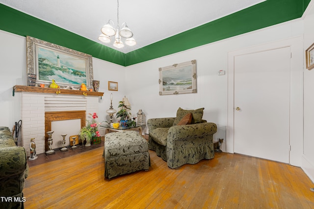 living area with a brick fireplace, hardwood / wood-style flooring, and an inviting chandelier