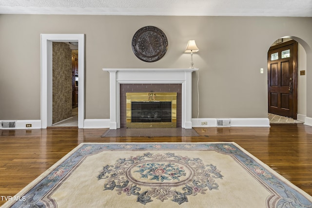 unfurnished living room with dark wood-type flooring, a textured ceiling, and a brick fireplace