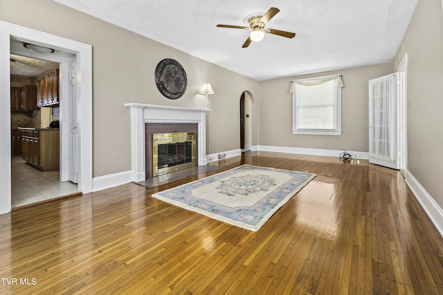 unfurnished living room featuring a textured ceiling, light hardwood / wood-style floors, a brick fireplace, and ceiling fan