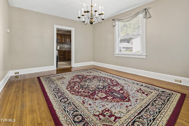 spare room with a textured ceiling, dark hardwood / wood-style flooring, and a notable chandelier