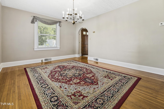 unfurnished room with wood-type flooring, a textured ceiling, and a chandelier