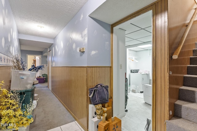 corridor featuring a textured ceiling, washing machine and clothes dryer, and wooden walls