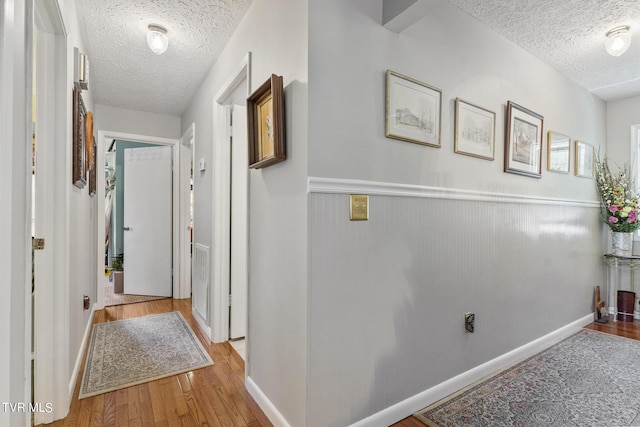 corridor with a textured ceiling and light hardwood / wood-style flooring