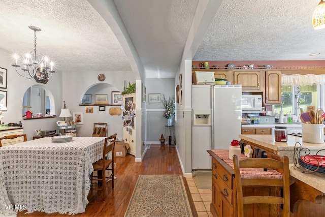 kitchen with decorative light fixtures, a textured ceiling, a notable chandelier, white appliances, and light hardwood / wood-style floors