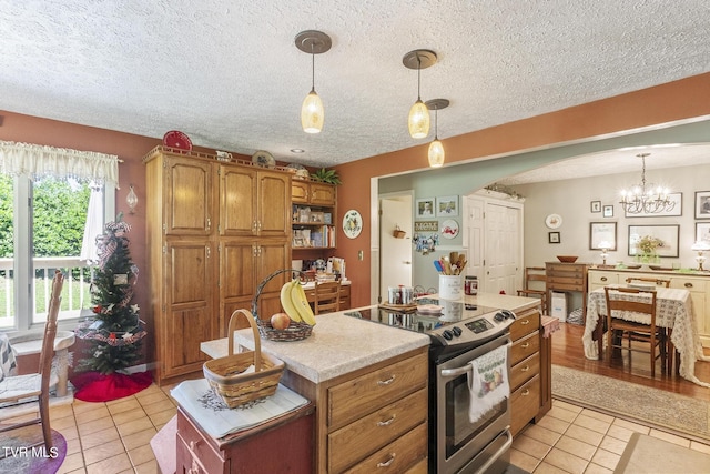 kitchen with a kitchen island, decorative light fixtures, light tile patterned floors, and stainless steel range with electric stovetop