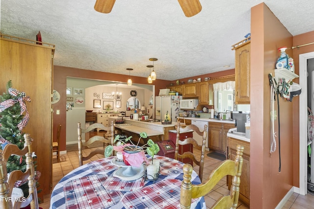 dining room featuring ceiling fan with notable chandelier, a textured ceiling, and light tile patterned flooring