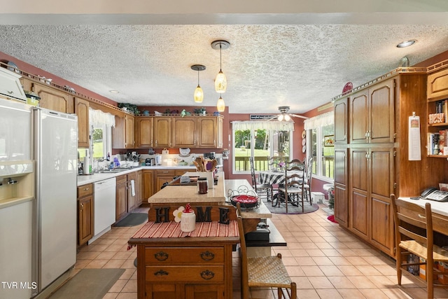 kitchen with light tile patterned floors, white appliances, hanging light fixtures, a wealth of natural light, and a kitchen island