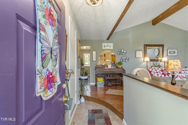 tiled entryway with a textured ceiling and vaulted ceiling with beams