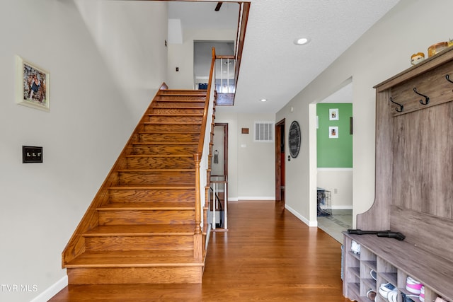 stairway featuring a textured ceiling, visible vents, recessed lighting, wood finished floors, and baseboards