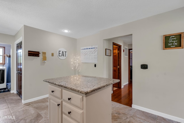 kitchen with a textured ceiling, light stone counters, baseboards, and a kitchen island
