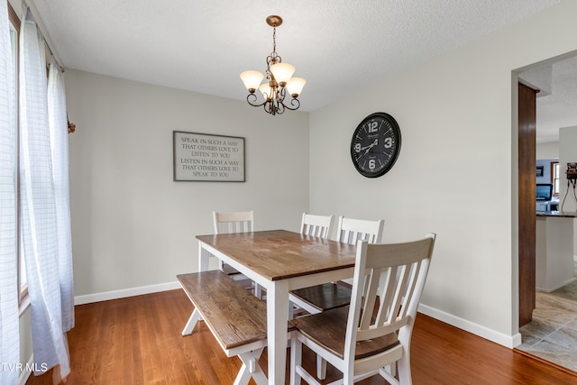 dining area with a chandelier, baseboards, a textured ceiling, and wood finished floors