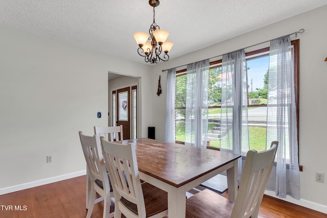 dining area with a textured ceiling, wood finished floors, an inviting chandelier, and baseboards