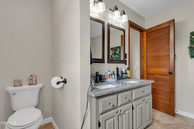bathroom featuring baseboards, double vanity, a textured ceiling, toilet, and a sink