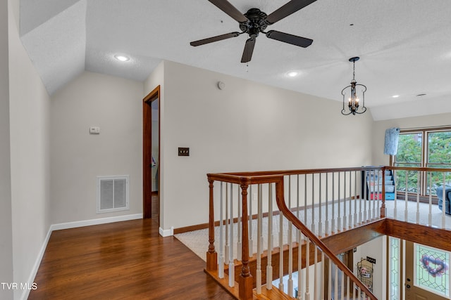 hall featuring visible vents, baseboards, an upstairs landing, a textured ceiling, and wood finished floors