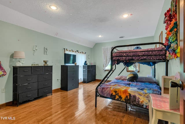 bedroom with wood-type flooring, baseboards, a textured ceiling, and lofted ceiling