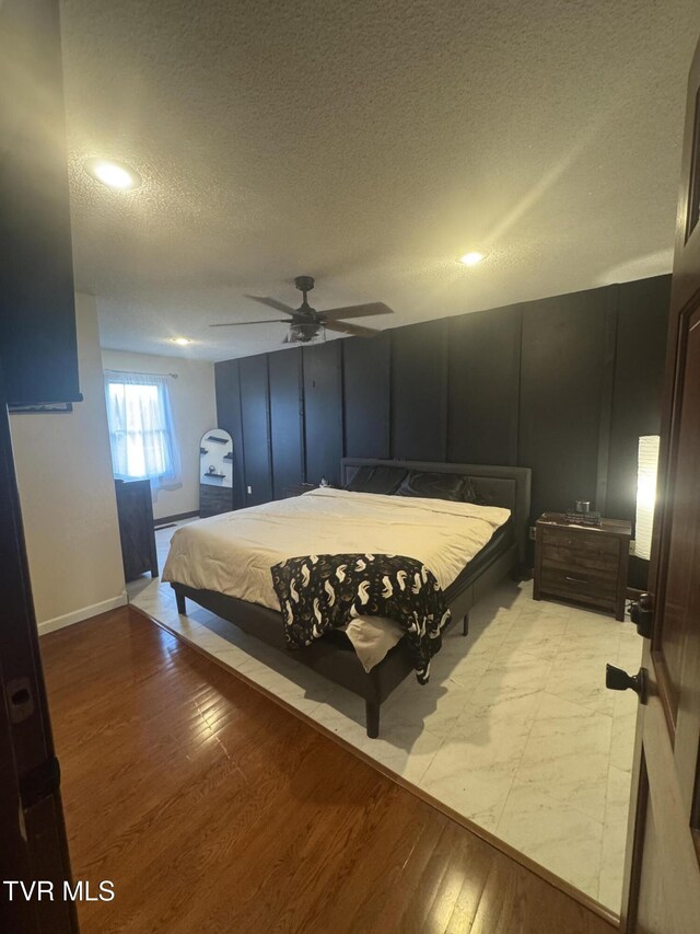 bedroom with ceiling fan, light wood finished floors, baseboards, and a textured ceiling