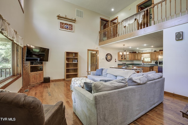 living room with light wood-type flooring, a towering ceiling, sink, and an inviting chandelier