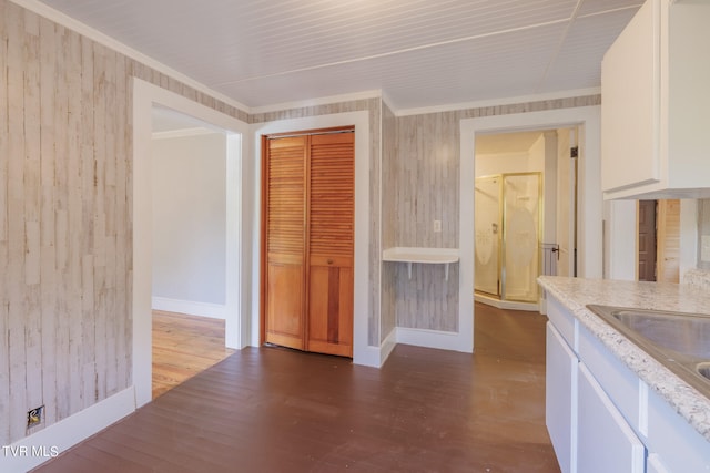 kitchen featuring wood walls, white cabinetry, hardwood / wood-style floors, ornamental molding, and light stone countertops