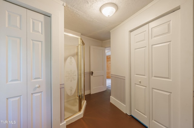 hall with a textured ceiling, ornamental molding, and dark wood-type flooring