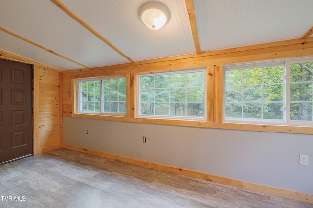 unfurnished room featuring wood walls, vaulted ceiling, and a healthy amount of sunlight