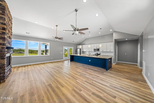 unfurnished living room featuring light hardwood / wood-style floors, high vaulted ceiling, a fireplace, ceiling fan, and sink