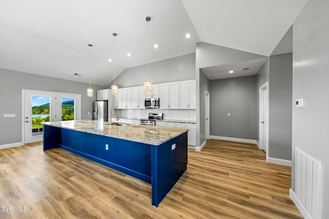 kitchen with light hardwood / wood-style floors, a large island with sink, white cabinetry, appliances with stainless steel finishes, and a kitchen bar