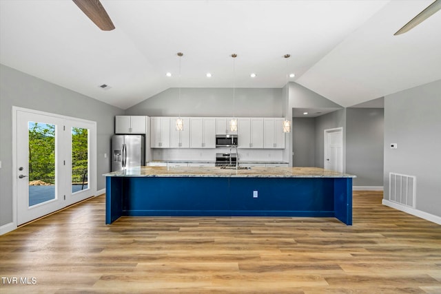 kitchen with appliances with stainless steel finishes, hanging light fixtures, white cabinetry, and light hardwood / wood-style flooring