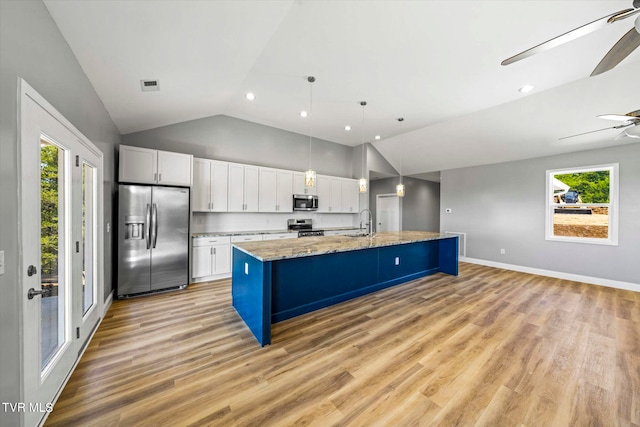 kitchen featuring appliances with stainless steel finishes, vaulted ceiling, an island with sink, white cabinets, and light wood-type flooring