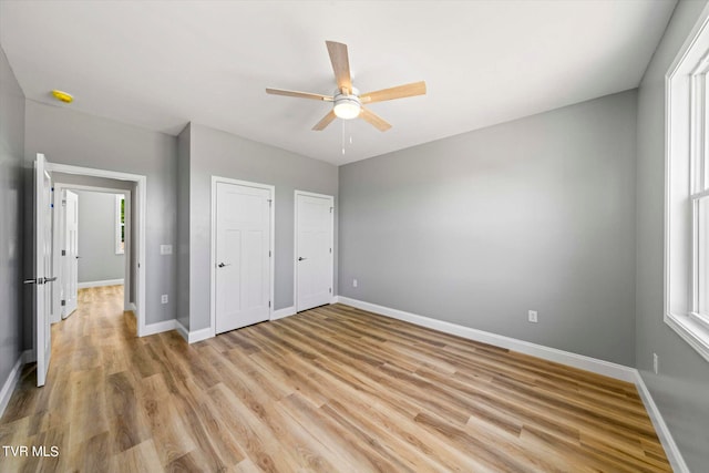 unfurnished bedroom featuring ceiling fan, light hardwood / wood-style flooring, and two closets