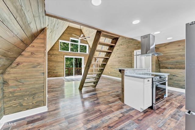 kitchen with island exhaust hood, appliances with stainless steel finishes, light stone counters, wooden walls, and white cabinetry