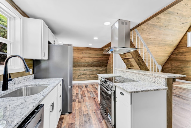 kitchen with island range hood, stainless steel appliances, wooden walls, sink, and white cabinetry