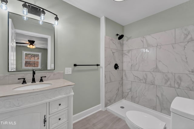 bathroom featuring a tile shower, vanity, toilet, and ceiling fan