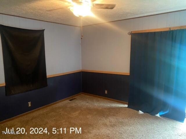 carpeted spare room with wood walls, ceiling fan, and a textured ceiling