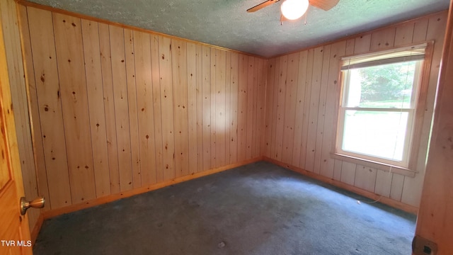 empty room with ceiling fan, wooden walls, dark carpet, and a textured ceiling