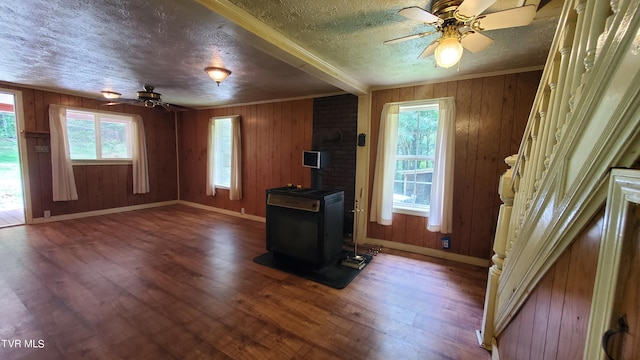 living room with wood-type flooring, a wood stove, ornamental molding, ceiling fan, and a textured ceiling