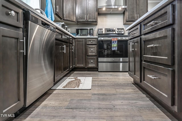 kitchen with fridge, dark brown cabinets, wall chimney exhaust hood, and stainless steel range with electric stovetop