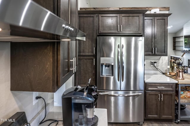 kitchen with stainless steel fridge, tasteful backsplash, dark brown cabinetry, lofted ceiling, and range hood