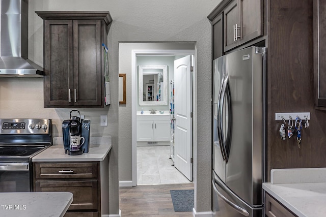 kitchen with light wood-type flooring, appliances with stainless steel finishes, dark brown cabinetry, and wall chimney range hood