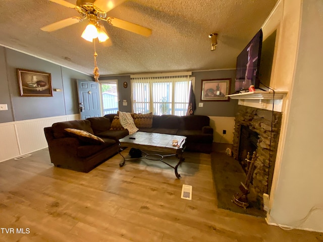 living room featuring ceiling fan, hardwood / wood-style flooring, a textured ceiling, and a fireplace