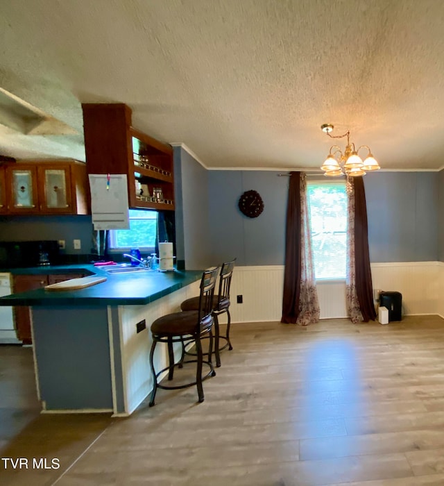 kitchen with light wood-type flooring, a chandelier, a textured ceiling, hanging light fixtures, and kitchen peninsula